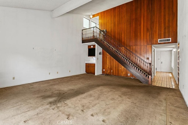 3431 Caspian Ave, Long Beach, CA 90810 - unfurnished living room featuring stairs, carpet floors, a high ceiling, beamed ceiling, and wooden walls