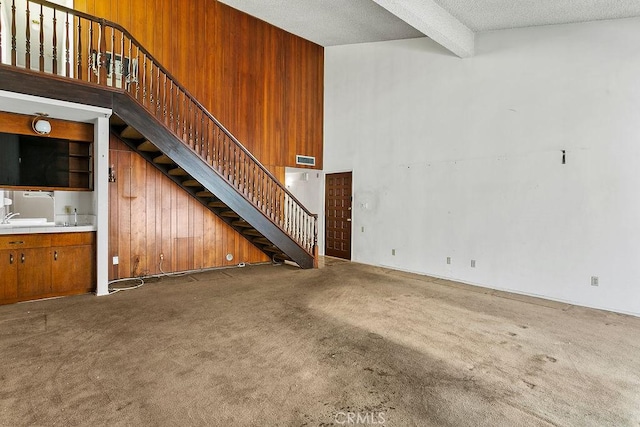 3431 Caspian Ave, Long Beach, CA 90810 - unfurnished living room with beam ceiling, carpet floors, stairs, a textured ceiling, and wood walls