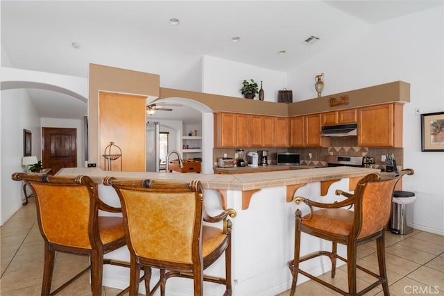 79140 Fred Waring Dr, Bermuda Dunes, CA 92203 - kitchen with tile countertops, under cabinet range hood, light tile patterned flooring, a breakfast bar area, and a towering ceiling