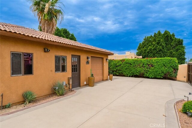 79140 Fred Waring Dr, Bermuda Dunes, CA 92203 - view of side of home featuring stucco siding, an attached garage, a tile roof, and driveway