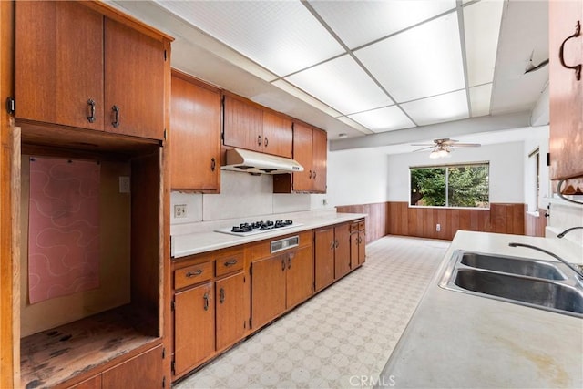 1305 S Westchester Dr, Anaheim, CA 92804 - kitchen featuring under cabinet range hood, wainscoting, brown cabinets, light countertops, and a ceiling fan