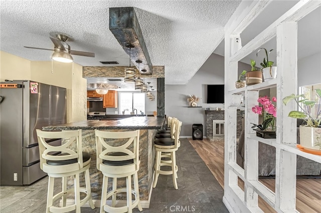 4883 E Geary St, Fresno, CA 93725 - kitchen featuring appliances with stainless steel finishes, a textured ceiling, dark countertops, a breakfast bar area, and ceiling fan