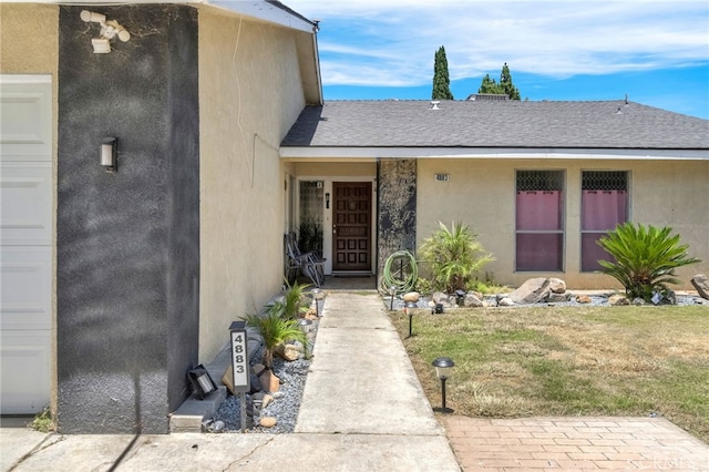 4883 E Geary St, Fresno, CA 93725 - view of exterior entry featuring stucco siding, a lawn, and a shingled roof