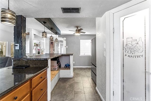 4883 E Geary St, Fresno, CA 93725 - kitchen with brown cabinetry, a textured ceiling, a ceiling fan, pendant lighting, and dark stone counters