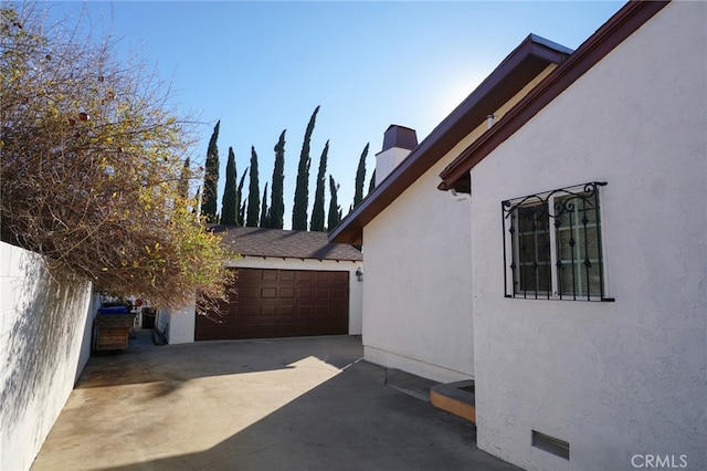 8937 Palmetto Ave, Fontana, CA 92335 - view of side of home featuring an attached garage, a chimney, driveway, and stucco siding