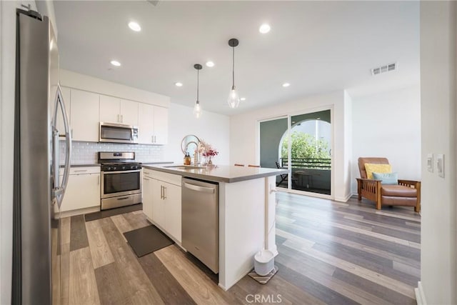117 N 5th St Unit B, Montebello, CA 90640 - kitchen featuring stainless steel appliances, wood finished floors, tasteful backsplash, white cabinetry, and a center island with sink