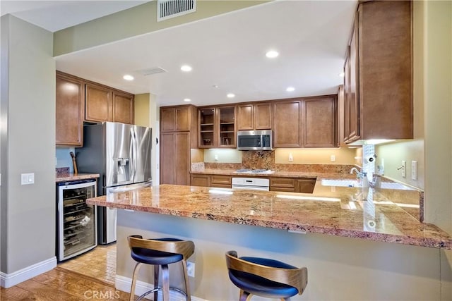 66 Glenalmond Ln, Ladera Ranch, CA 92694 - kitchen with stainless steel appliances, wine cooler, a peninsula, light stone counters, and glass insert cabinets