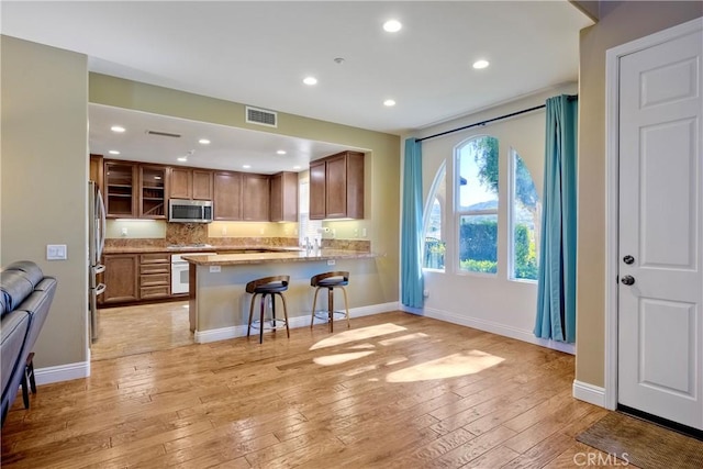 66 Glenalmond Ln, Ladera Ranch, CA 92694 - kitchen with appliances with stainless steel finishes, decorative backsplash, brown cabinetry, light wood-style floors, and a peninsula