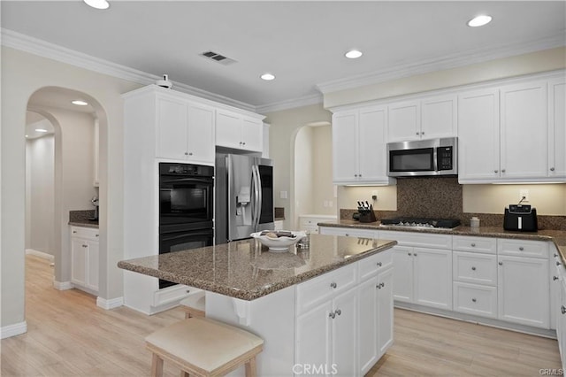 29851 Fox Creek Dr, Menifee, CA 92586 - kitchen featuring appliances with stainless steel finishes, arched walkways, dark stone countertops, a kitchen island, and white cabinetry