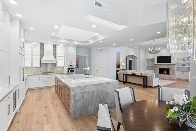 17124 Circa Oriente, Rancho Santa Fe, CA 92067 - kitchen featuring premium range hood, arched walkways, light wood-style flooring, recessed lighting, and light stone countertops