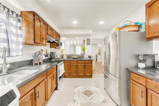 764 W 107th St, Los Angeles, CA 90044 - kitchen with appliances with stainless steel finishes, a peninsula, brown cabinetry, light tile patterned floors, and under cabinet range hood