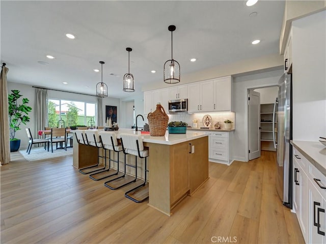 17151 Kent St, Hesperia, CA 92345 - kitchen with appliances with stainless steel finishes, recessed lighting, light wood-style flooring, a kitchen island with sink, and backsplash