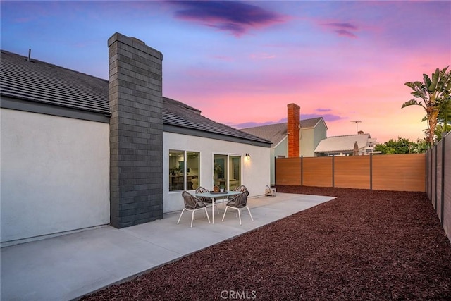39 Cape Cod, Irvine, CA 92620 - back of property at dusk with a chimney, a fenced backyard, stucco siding, and a patio