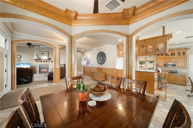 35655 52nd St E, Palmdale, CA 93552 - dining area with a ceiling fan, arched walkways, ornamental molding, a glass covered fireplace, and a wainscoted wall
