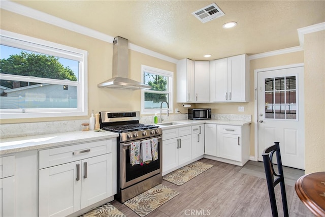 3704 La Sierra Ave, Riverside, CA 92505 - kitchen with gas stove, wall chimney range hood, black microwave, white cabinetry, and light wood-style flooring