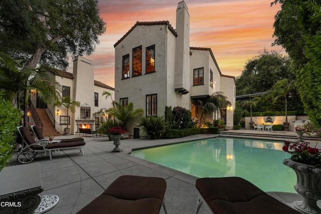 1205 Linda Vista Ave, Pasadena, CA 91103 - back of house at dusk featuring a patio, stucco siding, a lit fireplace, an outdoor pool, and stairs