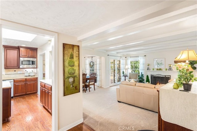 3191 Woodstock Rd, Rossmoor, CA 90720 - living room with a warm lit fireplace, light wood-style floors, beamed ceiling, and a skylight