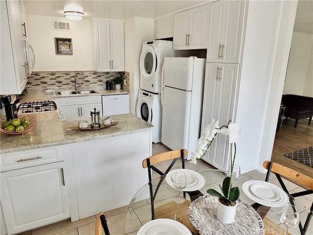 16573 Pescado Ln Unit 3A, Huntington Beach, CA 92649 - kitchen featuring white appliances, stacked washer / drying machine, white cabinetry, and tasteful backsplash