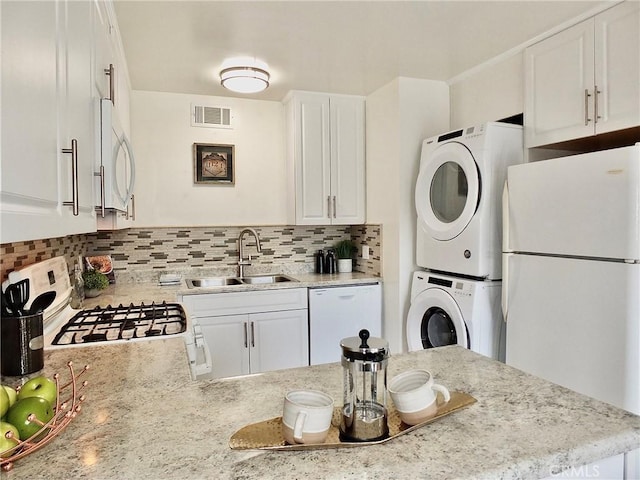 16573 Pescado Ln Unit 3A, Huntington Beach, CA 92649 - kitchen featuring white appliances, stacked washer / drying machine, backsplash, white cabinetry, and a peninsula
