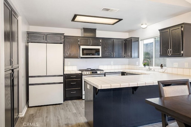 1085 Admiral Ln, Chico, CA 95973 - kitchen with white appliances, a peninsula, tile countertops, light wood-style floors, and a kitchen bar