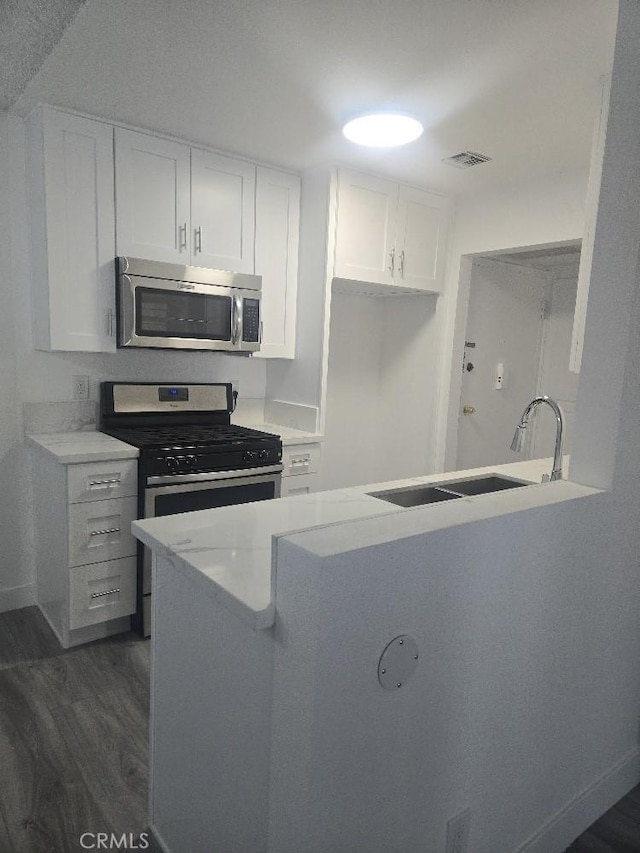 21000 Parthenia St Unit 6, Canoga Park, CA 91304 - kitchen with stainless steel appliances, dark wood finished floors, white cabinetry, light countertops, and a peninsula