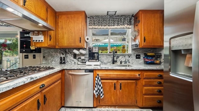 8356 Bella Vista Dr, Rancho Cucamonga, CA 91701 - kitchen with appliances with stainless steel finishes, under cabinet range hood, brown cabinetry, tasteful backsplash, and light stone countertops