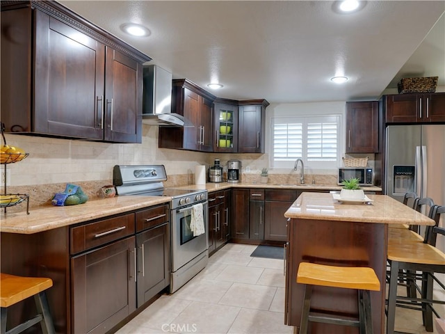 21829 Legend Ave, Carson, CA 90745 - kitchen featuring appliances with stainless steel finishes, wall chimney exhaust hood, a breakfast bar area, tasteful backsplash, and light stone countertops