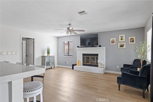 7209 Copper Creek Way, Bakersfield, CA 93308 - living room featuring a ceiling fan, light wood finished floors, a brick fireplace, and a textured ceiling