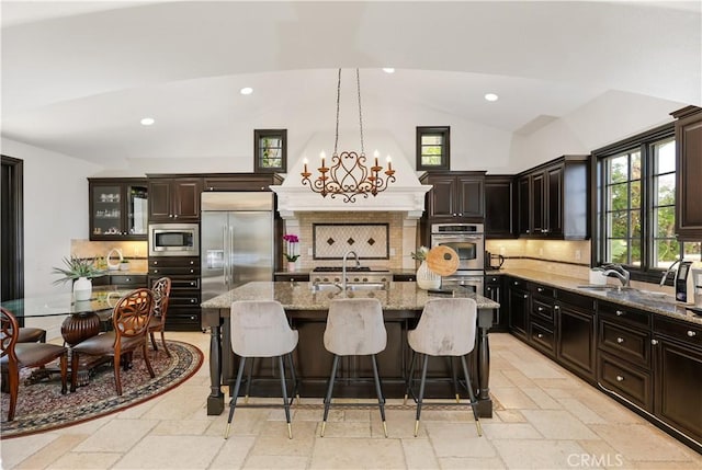 41 Balcony, Irvine, CA 92603 - kitchen featuring built in appliances, vaulted ceiling, stone tile floors, an island with sink, and decorative backsplash