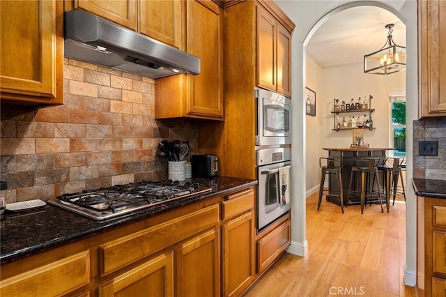 1968 Bancroft Dr, Chico, CA 95928 - kitchen featuring under cabinet range hood, stainless steel appliances, brown cabinets, and tasteful backsplash