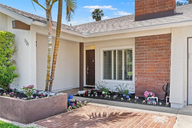 3125 Yukon Ave, Costa Mesa, CA 92626 - view of exterior entry featuring roof with shingles, brick siding, a chimney, and stucco siding