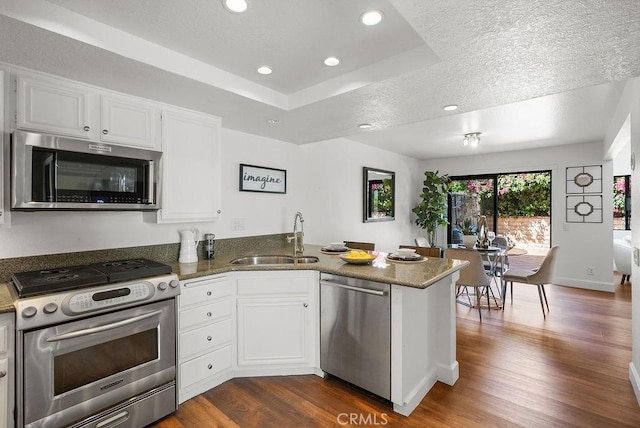 24511 Sutton Ln, Laguna Niguel, CA 92677 - kitchen with appliances with stainless steel finishes, a peninsula, white cabinets, dark wood-style floors, and dark stone countertops