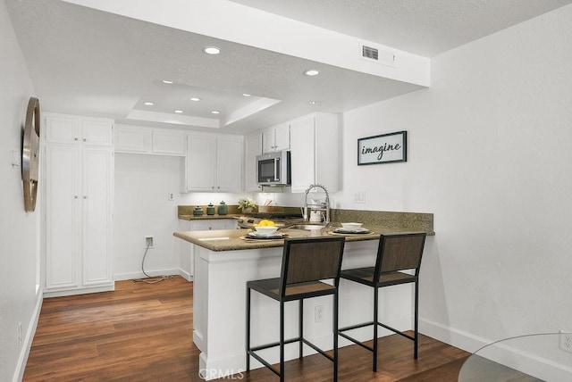 24511 Sutton Ln, Laguna Niguel, CA 92677 - kitchen with stainless steel microwave, a peninsula, white cabinetry, dark wood-style flooring, and recessed lighting