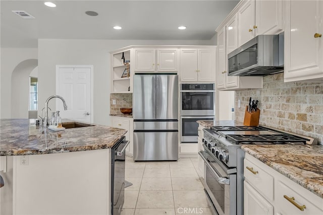 1775 Honors Ln, Corona, CA 92883 - kitchen with appliances with stainless steel finishes, arched walkways, open shelves, dark stone countertops, and white cabinetry