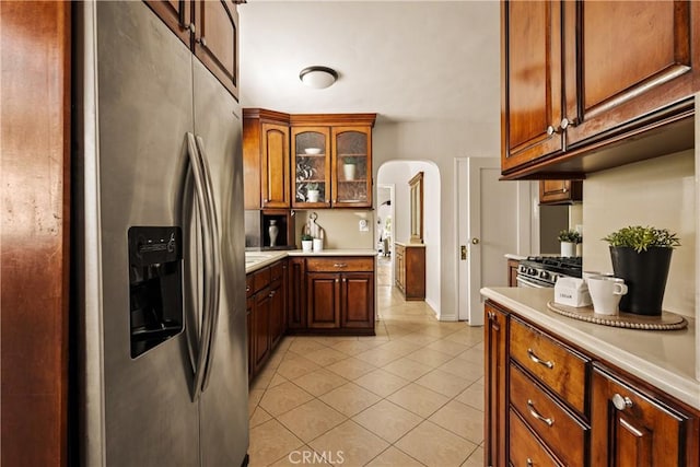 3848 Boyce Ave, Los Angeles, CA 90039 - kitchen featuring appliances with stainless steel finishes, light countertops, light tile patterned flooring, arched walkways, and glass insert cabinets
