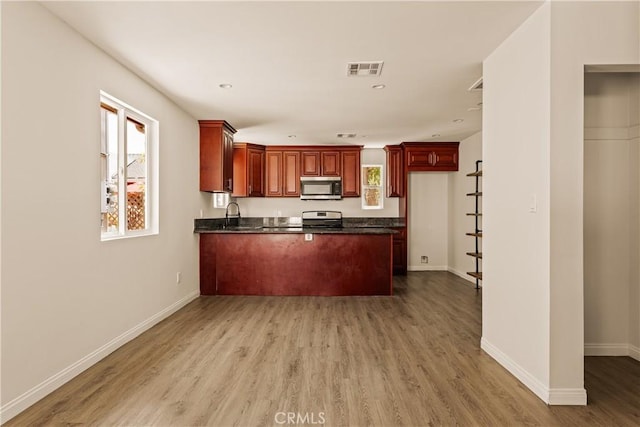 3848 Boyce Ave, Los Angeles, CA 90039 - kitchen featuring appliances with stainless steel finishes, dark countertops, a peninsula, light wood-style floors, and reddish brown cabinets
