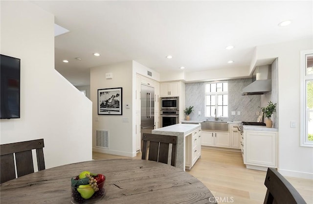 2534 Bungalow Pl Unit 87, Corona Del Mar, CA 92625 - kitchen featuring wall chimney range hood, appliances with stainless steel finishes, decorative backsplash, white cabinets, and a center island