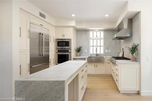 2534 Bungalow Pl Unit 87, Corona Del Mar, CA 92625 - kitchen with built in appliances, wall chimney exhaust hood, backsplash, light wood-type flooring, and white cabinetry