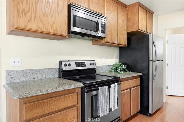 1206 E Vine Ave, West Covina, CA 91790 - kitchen featuring appliances with stainless steel finishes, light wood finished floors, light stone counters, and brown cabinetry