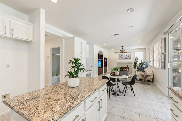 4262 Havenridge, Corona, CA 92883 - kitchen featuring a ceiling fan, a lit fireplace, white cabinetry, light stone countertops, and a center island