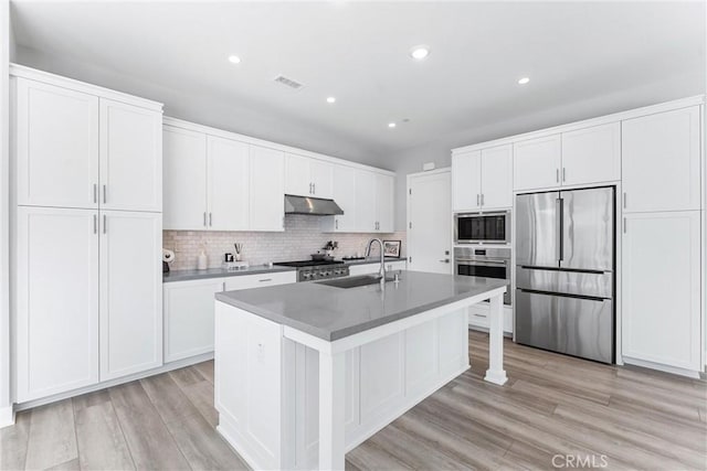 183 Plum Lily, Irvine, CA 92618 - kitchen featuring stainless steel appliances, under cabinet range hood, a center island with sink, white cabinets, and tasteful backsplash