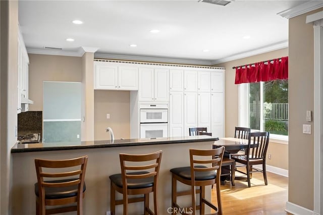 21658 Canyon Heights Cir, Saugus, CA 91390 - kitchen featuring double oven, ornamental molding, white cabinetry, a peninsula, and light wood-type flooring
