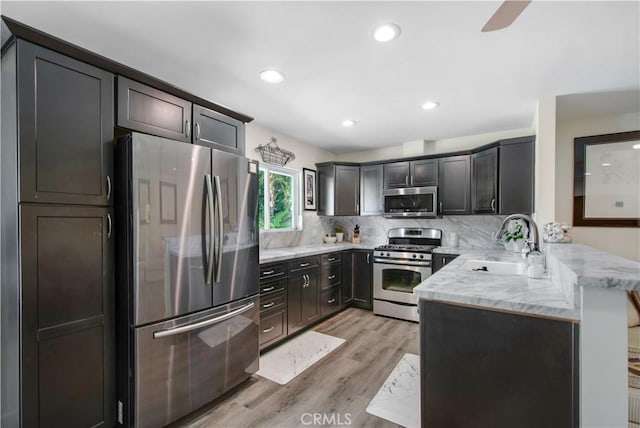 1212 Dover Dr, Newport Beach, CA 92660 - kitchen with stainless steel appliances, a peninsula, light wood-style floors, decorative backsplash, and light stone countertops