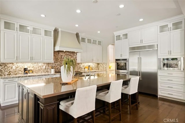 2282 E Rosecrans Ct, Brea, CA 92821 - kitchen with stainless steel appliances, custom range hood, a kitchen island with sink, dark wood-type flooring, and tasteful backsplash