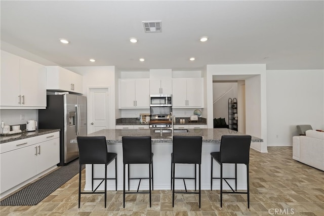 27240 Lost Palm St, Menifee, CA 92585 - kitchen with appliances with stainless steel finishes, a breakfast bar area, white cabinetry, an island with sink, and dark stone counters