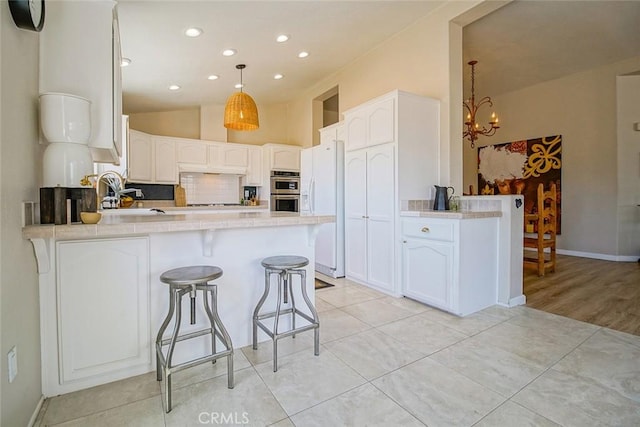 1001 Gibralter Rd, Landers, CA 92285 - kitchen featuring a peninsula, a chandelier, white fridge with ice dispenser, light countertops, and white cabinets
