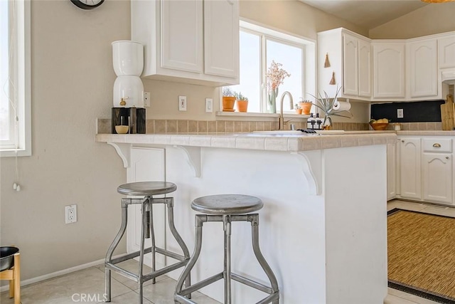1001 Gibralter Rd, Landers, CA 92285 - kitchen featuring white cabinets, a kitchen breakfast bar, tile countertops, and vaulted ceiling