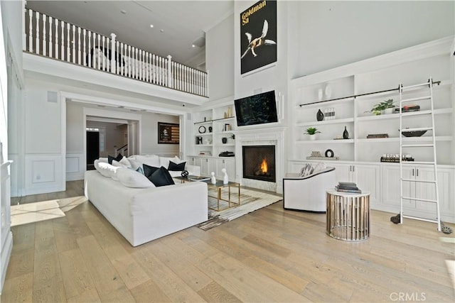 17528 Jayden Ln, Encino, CA 91316 - living room featuring built in features, a warm lit fireplace, a high ceiling, wood finished floors, and a wainscoted wall