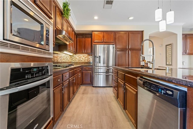 28549 Oakhurst Way, Temecula, CA 92591 - kitchen featuring stainless steel appliances, crown molding, under cabinet range hood, arched walkways, and light wood-style floors