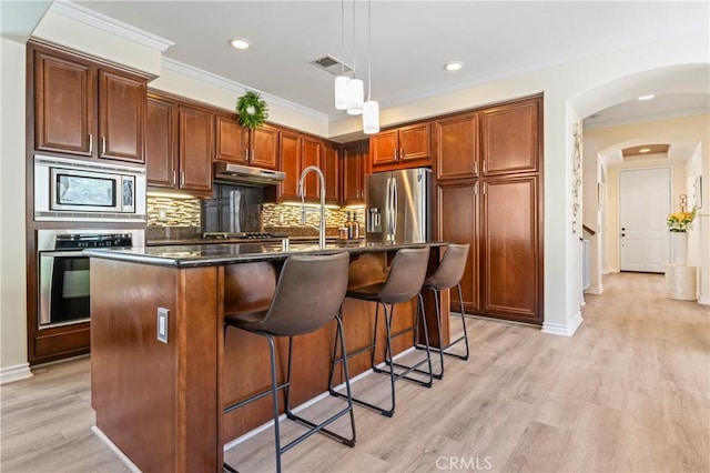 28549 Oakhurst Way, Temecula, CA 92591 - kitchen featuring appliances with stainless steel finishes, under cabinet range hood, dark countertops, light wood-style floors, and arched walkways